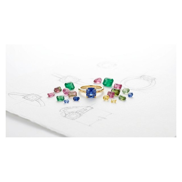 Loose coloured gemstones scattered around a finished bespoke gold ring on a design sketch