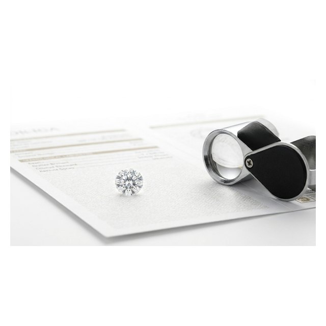 A loose diamond resting on a gemmological laboratory certificate with a loupe