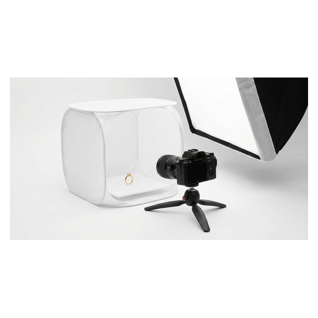 A camera on a tripod photographing a gold ring in a white light tent