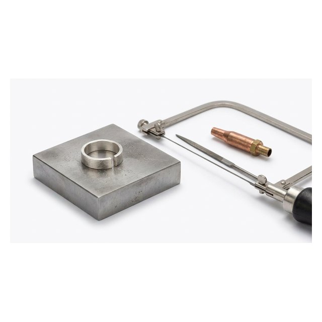 A half-finished silver ring with jeweller's saw, file and torch on a bench block