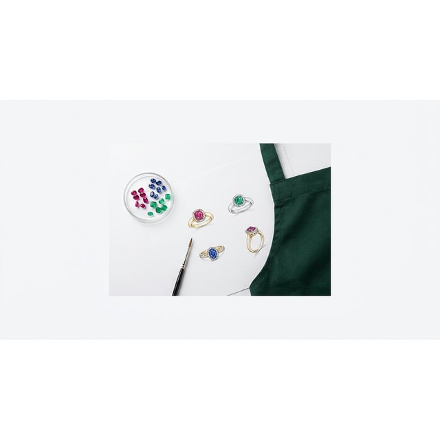 A jewellery designer's workspace with colour renderings, loose gems and a fine brush
