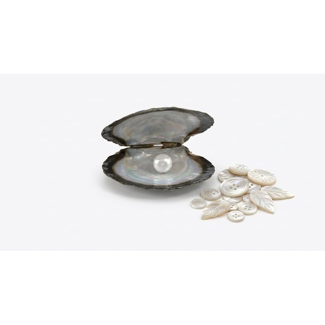 An opened oyster shell with a pearl beside mother-of-pearl buttons and pieces