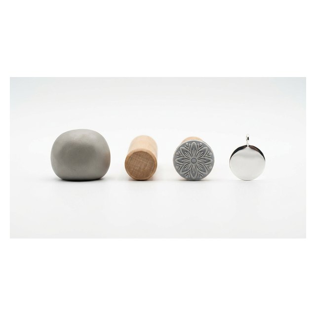 Unfired silver clay with roller and stamp beside a finished polished pure-silver pendant